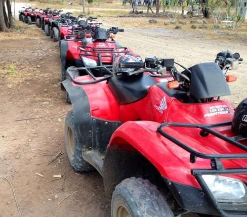 Row of muddy red ATVs parked along a dirt road at the start of a tour