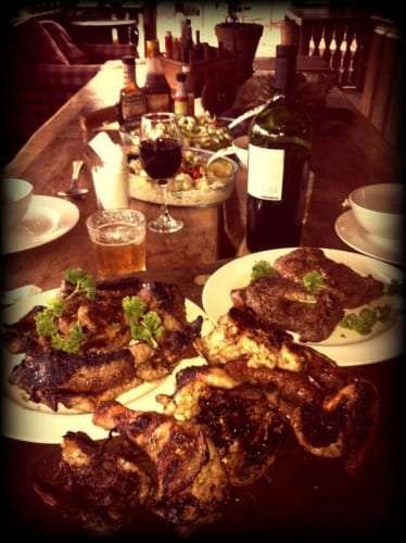 Dinner table with grilled chicken and steak, a glass of wine and a bottle