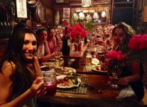 Group of women sharing dinner at a long table with red flowers and drinks