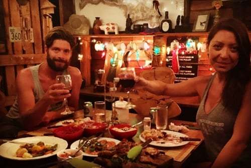 Couple smiling at a candlelit table with a glass of wine and plates of grilled food