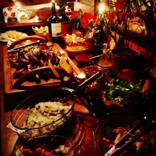 Wooden board of grilled meats beside bowls of rice and salad on a candlelit table
