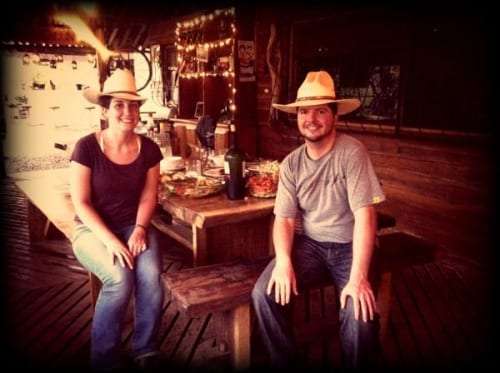 Man and woman in straw hats seated on a bench at a wooden dining table