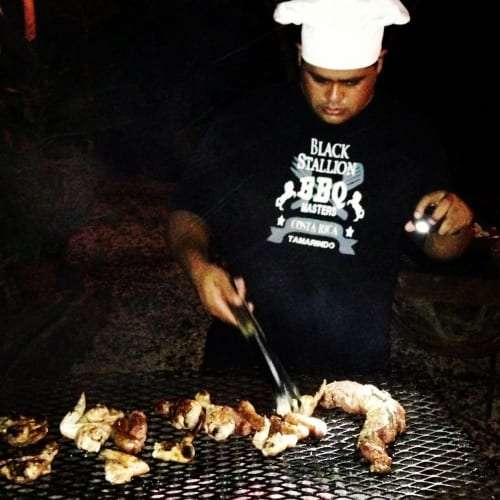 Chef in a white hat and Black Stallion BBQ Masters shirt grilling meat at night