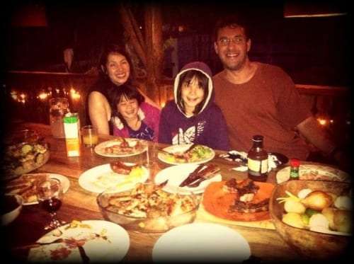 Family of four seated at a dinner table with plates of grilled meat and potatoes