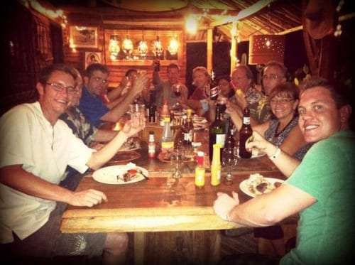 Smiling group of diners around a wooden table with bottles and plates