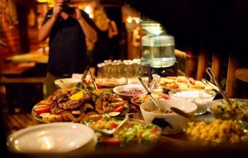 Buffet of grilled meat, salads and rice with a guest taking a photo behind it