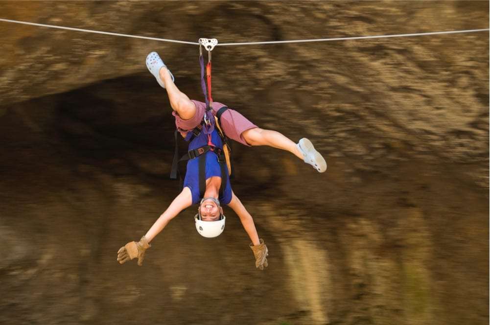 Smiling woman hanging upside down from a zip line in front of a rock wall