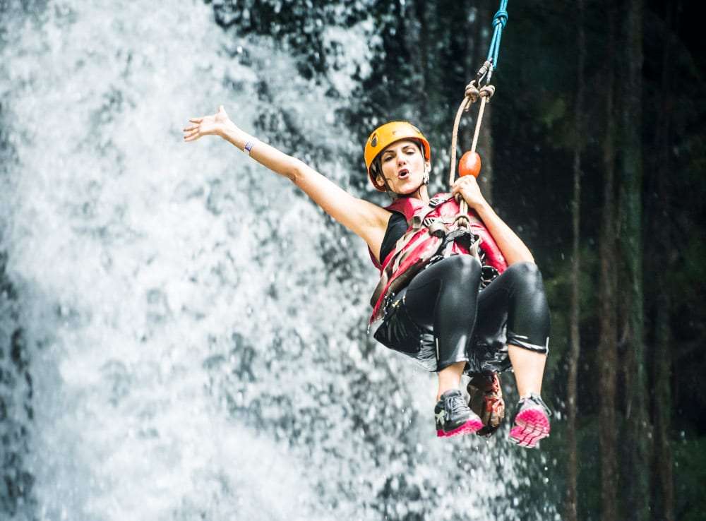 Woman in an orange helmet and harness rappelling down a waterfall