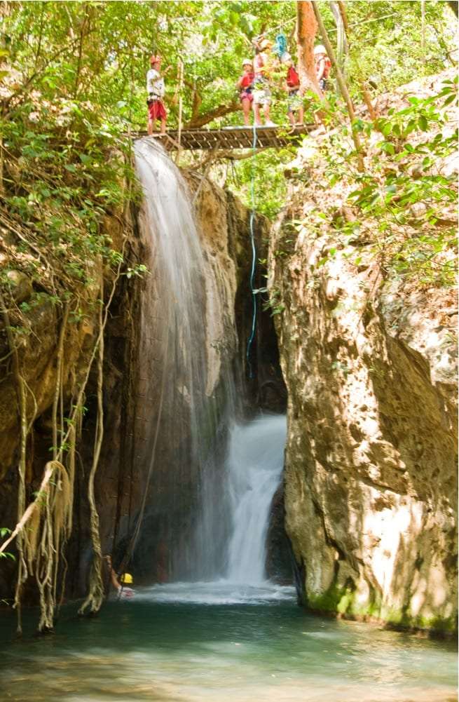 Guests standing on a wooden platform above a waterfall that drops into a turquoise pool