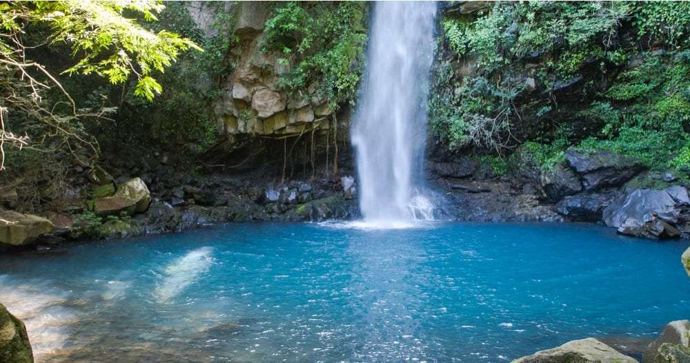 Waterfall dropping into a bright blue pool surrounded by green rocks and trees