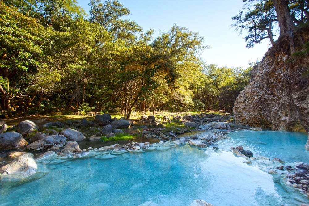 Turquoise river pool with rocks and sunlit trees along the bank