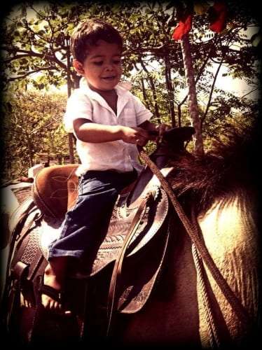 Young child in a white shirt sitting on a saddled horse