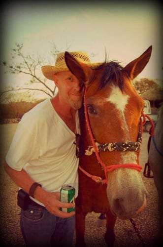 Man in a straw hat leaning his cheek against a brown horse with a red halter
