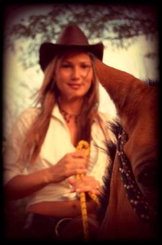 Woman in a brown hat holding a yellow rope beside the head of a horse