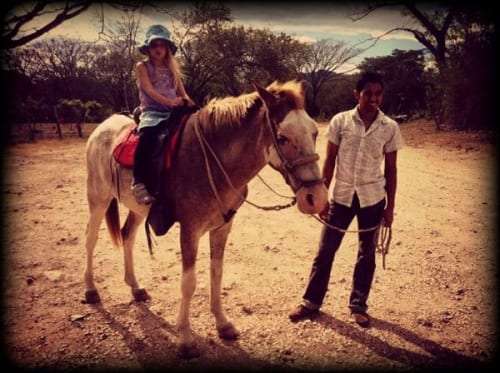 Girl in a bucket hat on a white horse with a guide holding the rope beside her