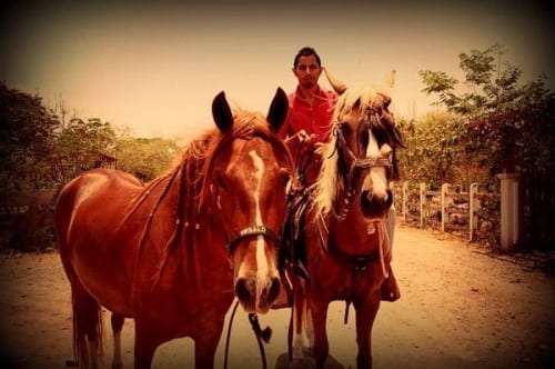 Man in a red shirt on horseback behind two horses on a rural dirt road