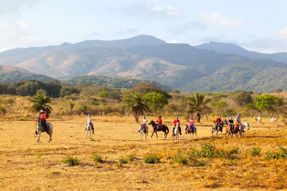Line of riders crossing an open field with a mountain range in the distance