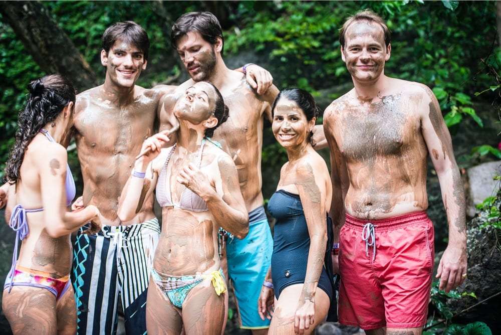Friends with mud on their faces and bodies posing in front of green leaves
