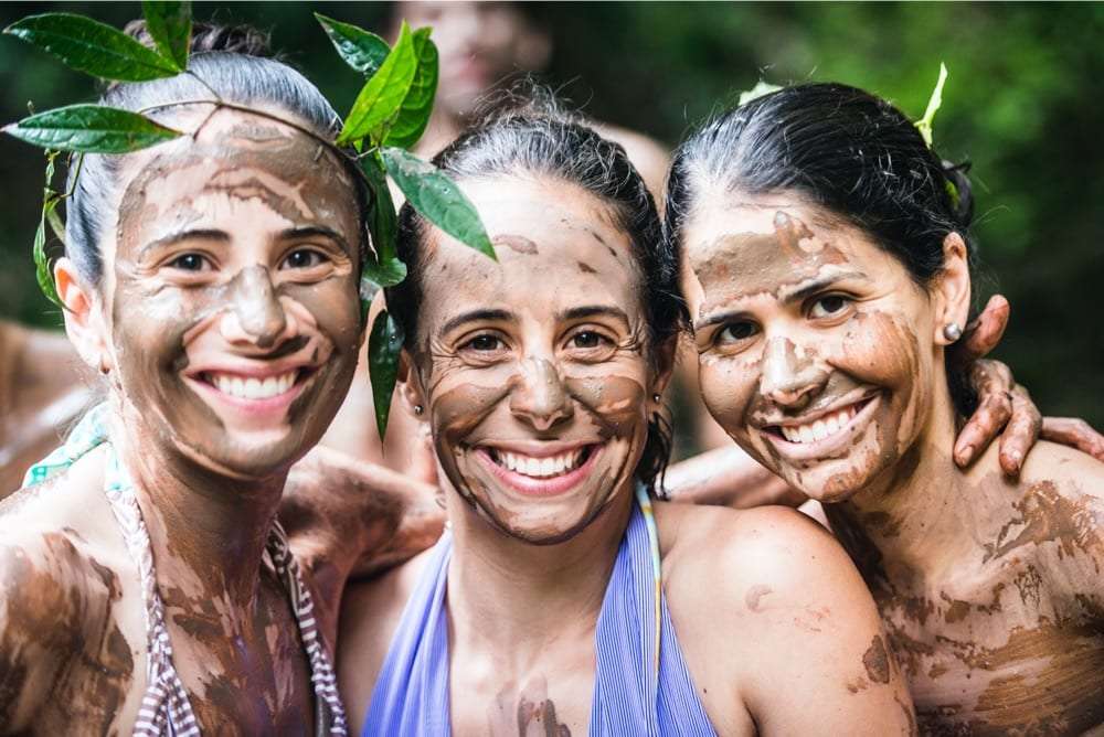 Close-up of three women laughing with mud masks on their faces