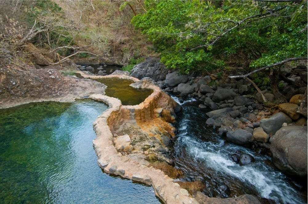 Natural hot spring pools beside a rocky stream and trees