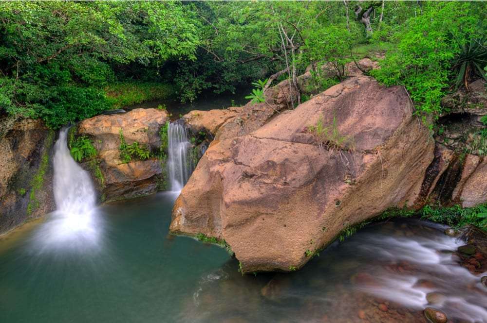 Two small waterfalls dropping into a green pool beside a large orange boulder