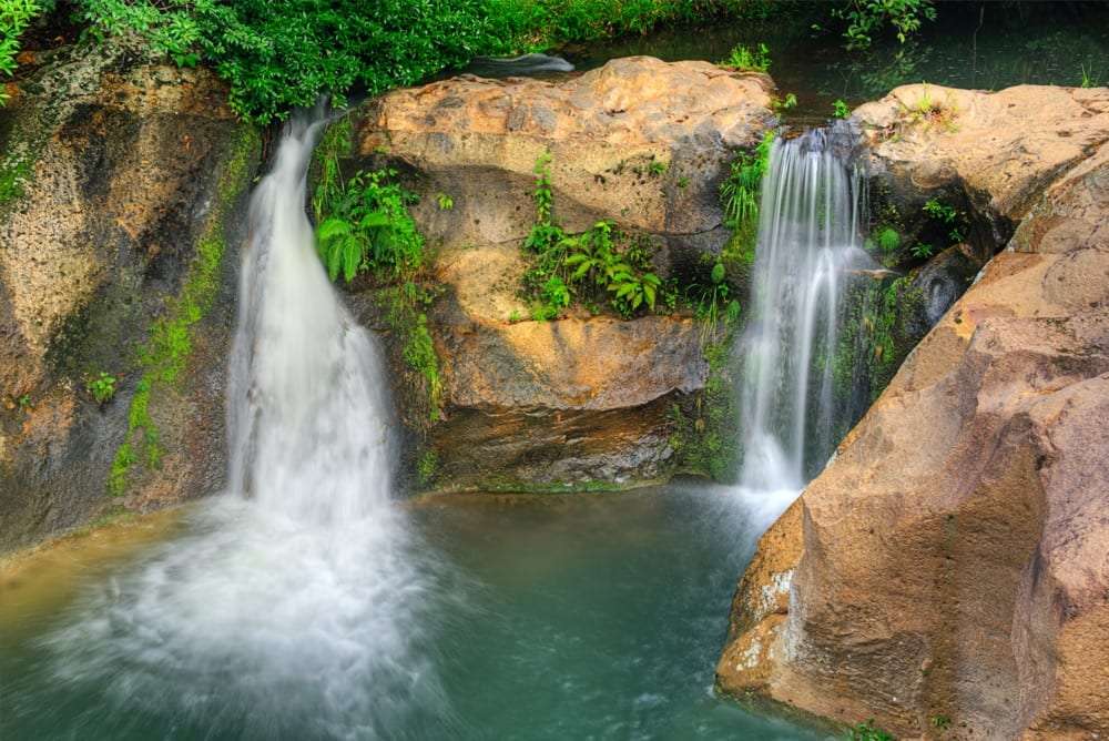 Two small waterfalls dropping into a green pool between mossy rocks
