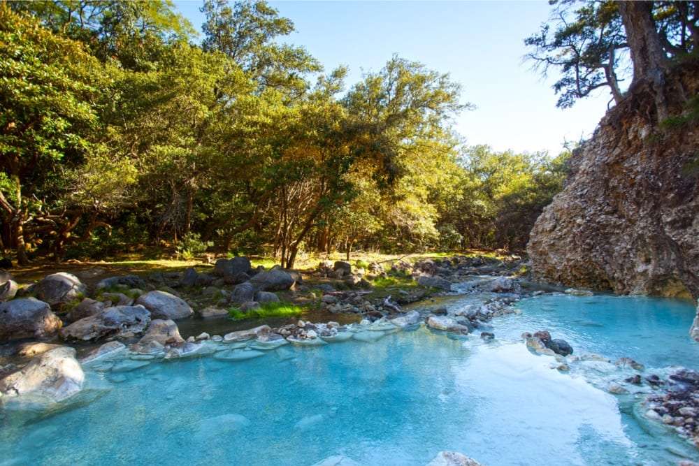 Turquoise thermal river pool with rocks and sunlit trees on the bank