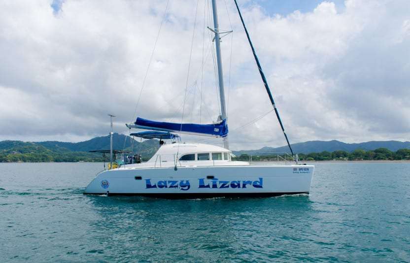 White Lazy Lizard catamaran on calm green water with hills and a cloudy sky behind