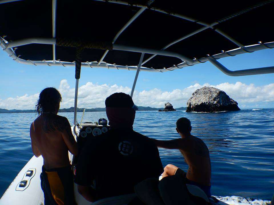 Passengers on an inflatable boat watching a rock outcrop rise from open water