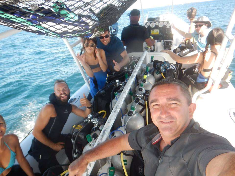 Divers and crew smiling on a dive boat with rows of scuba tanks in the middle