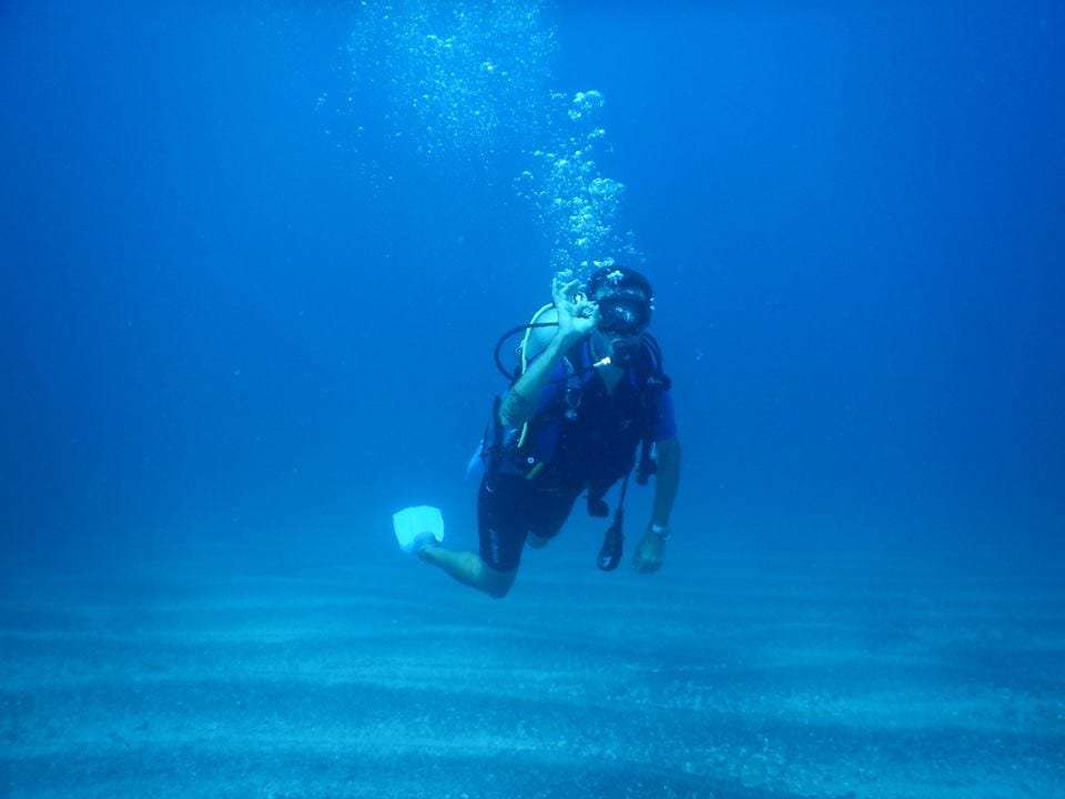 Scuba diver making an OK sign with bubbles rising in deep blue water