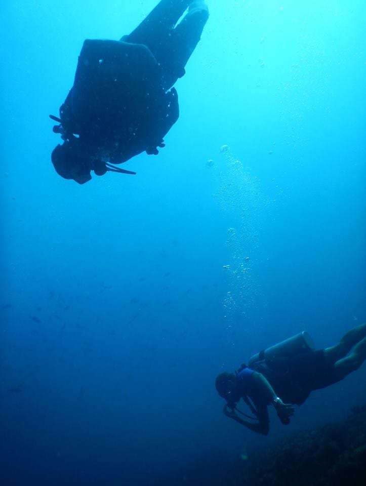 Two scuba divers swimming in blue water, one above and one below