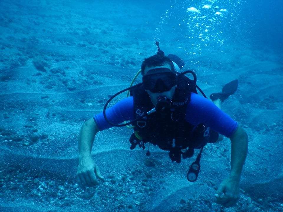 Scuba diver in a blue shirt swimming above a sandy seabed