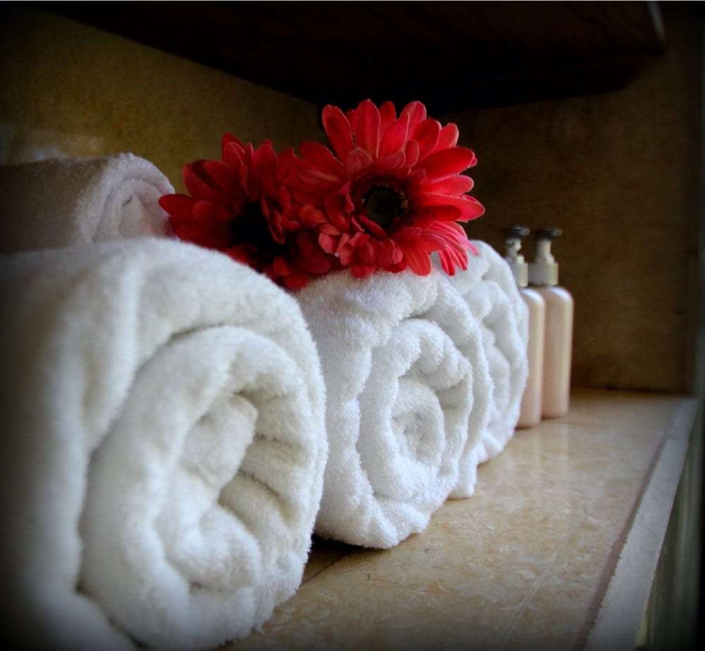 Rolled white towels topped with red gerbera flowers beside lotion bottles on a shelf