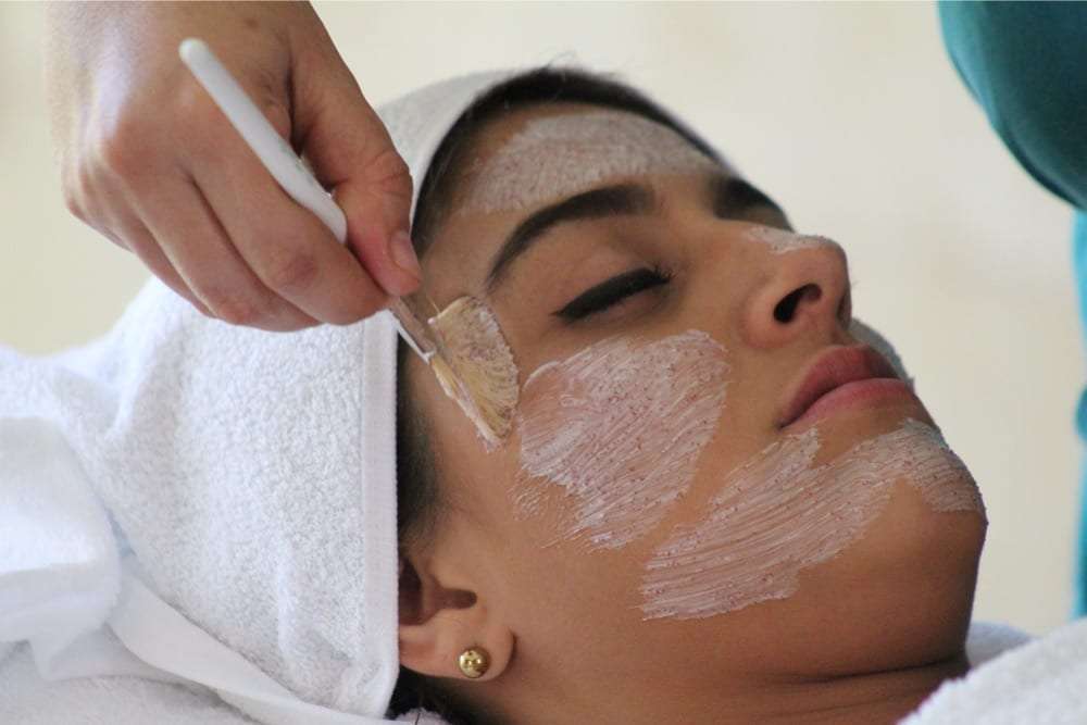 Woman lying with a towel around her hair as a facial mask is brushed on