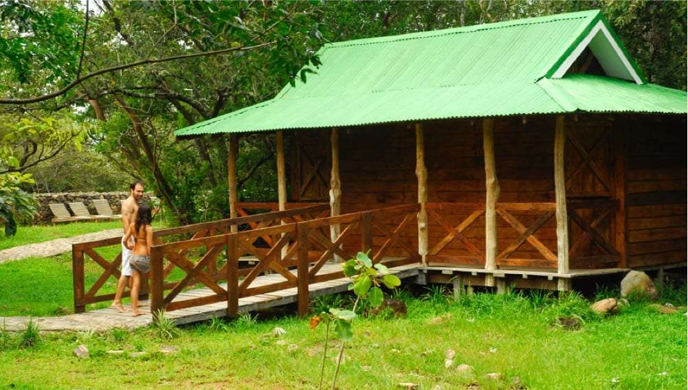Couple walking toward a wooden spa cabin with a green roof and railed walkway