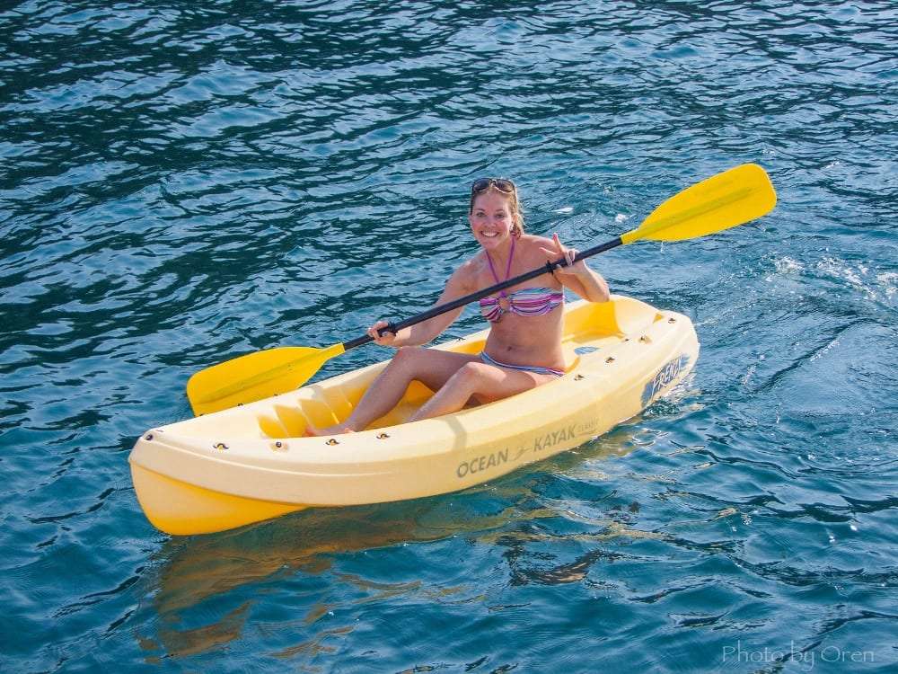 Smiling woman in a bikini paddling a yellow kayak on the sea