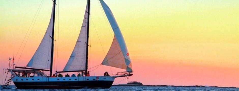 Two-masted sailboat under sail against an orange and pink sunset