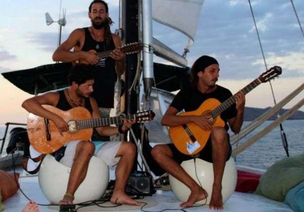 Three men playing acoustic guitars on the deck of a sailboat at dusk