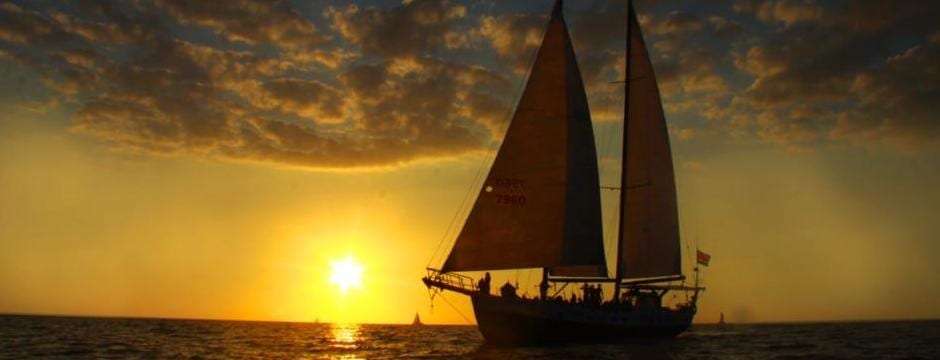 Silhouette of a two-masted sailboat against a golden setting sun