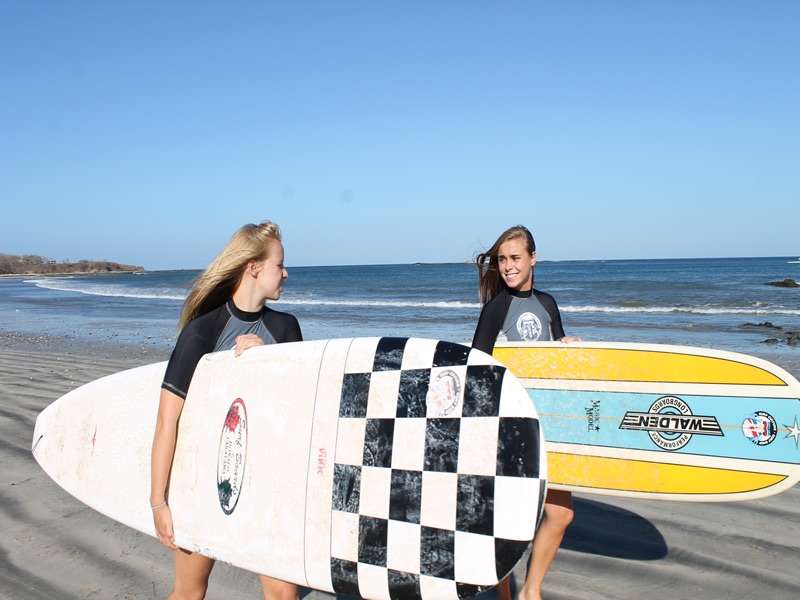 Two young women in rash guards carrying surfboards along a beach