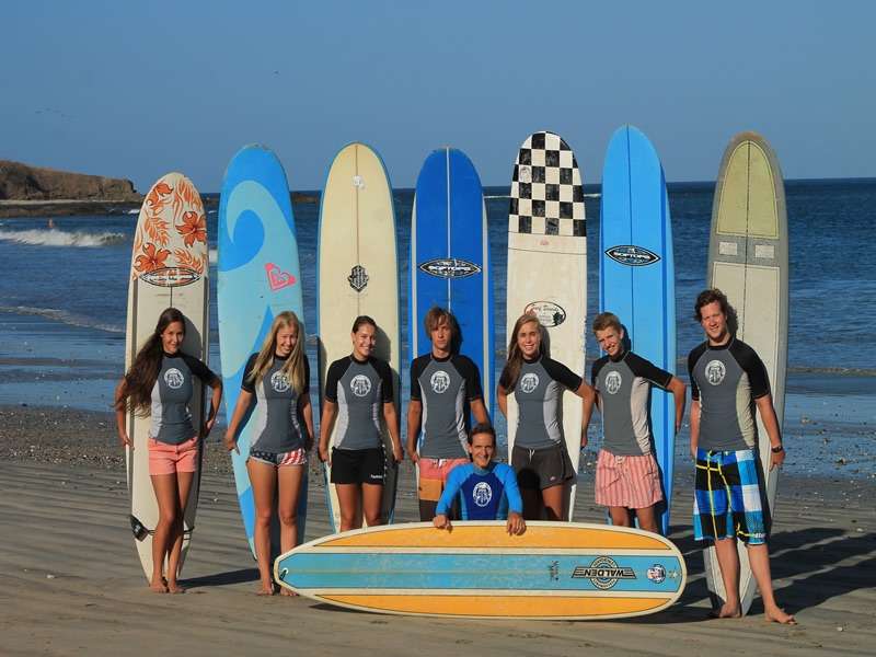 Group of surf students in matching rash guards posing in front of upright surfboards