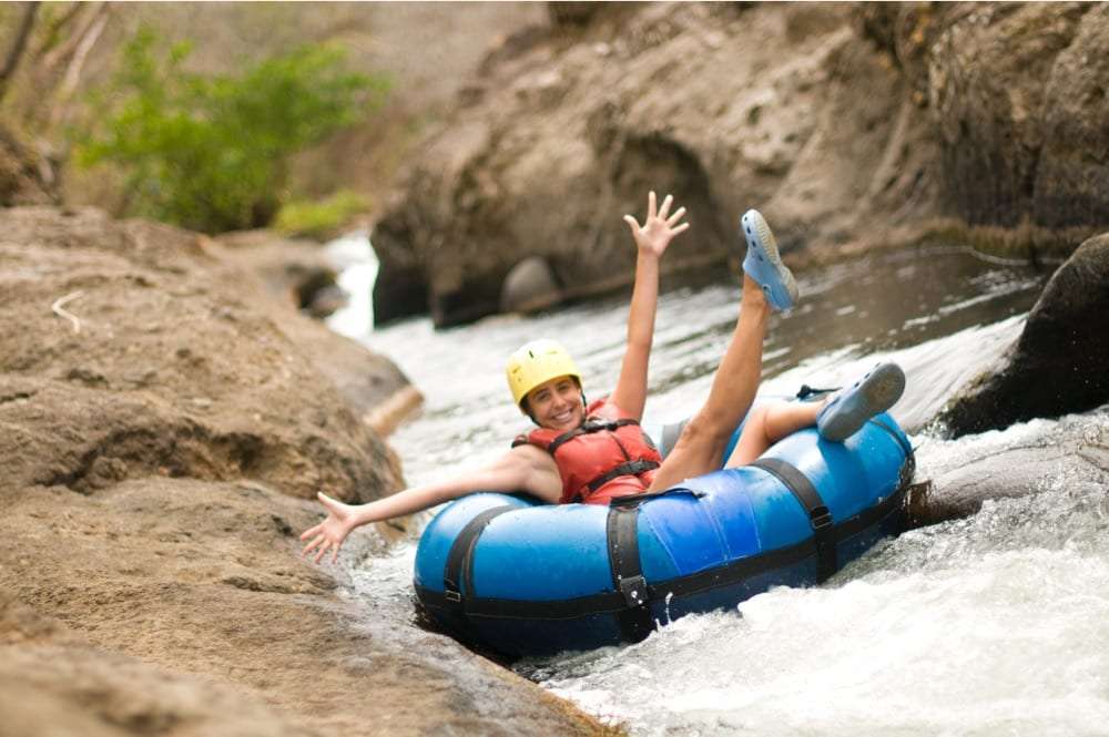 Smiling woman in a helmet and life vest riding a blue inner tube down a rocky river
