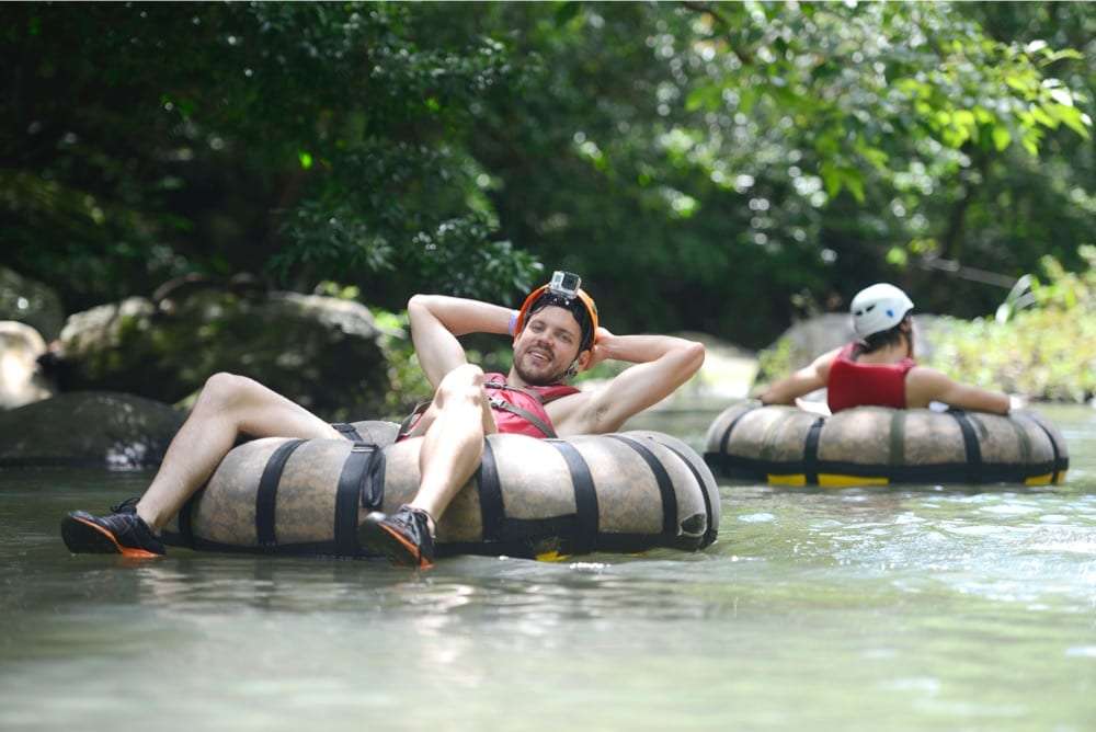 Man in a helmet with a camera relaxing with his hands behind his head on a camouflage tube on a calm river
