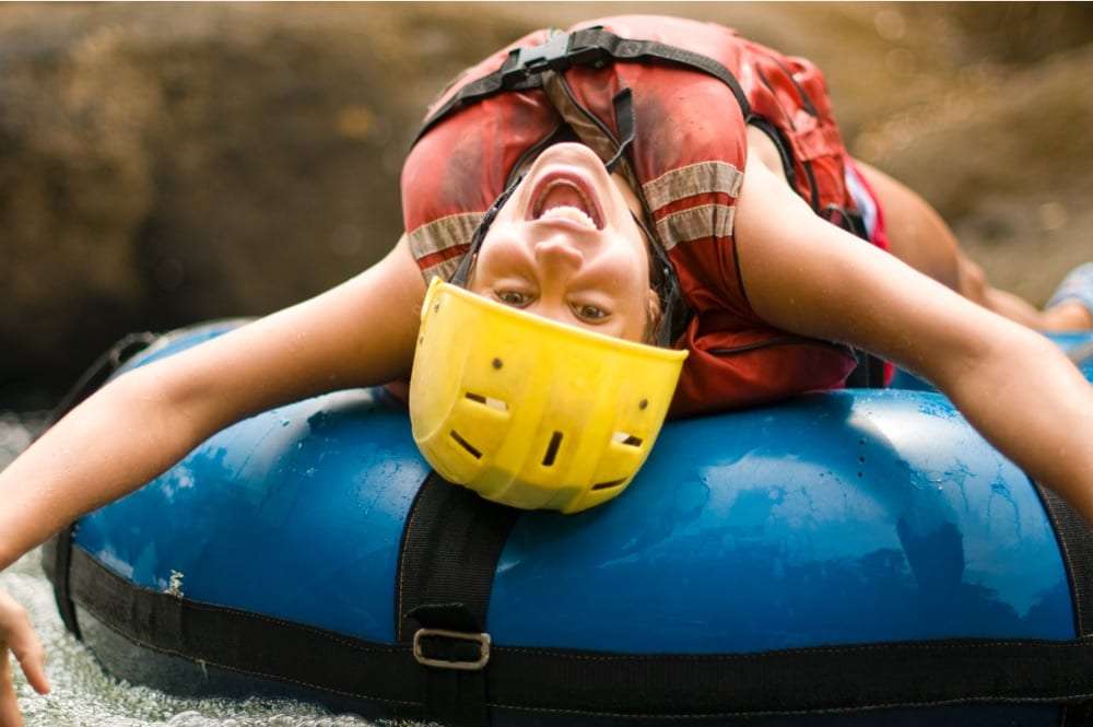 Smiling woman in a yellow helmet leaning backward over a blue river tube