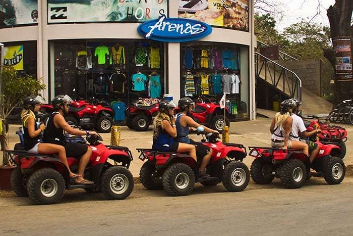 Four riders in helmets on red ATVs parked in front of the Arenas surf shop