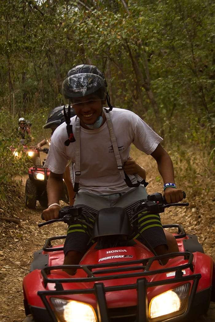 Smiling rider in a helmet and white T-shirt on a red Honda ATV on a forest trail