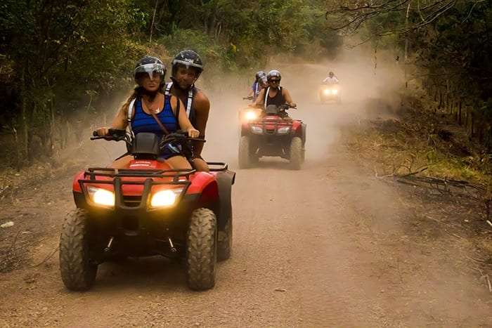 Red ATVs with helmeted riders driving along a dusty dirt road