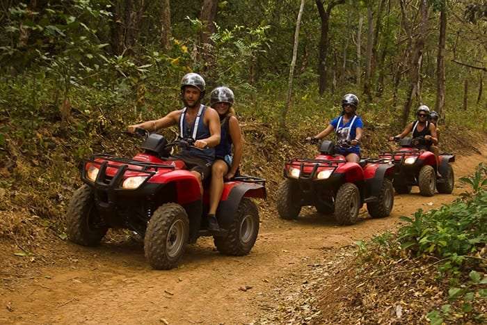 Group of riders on red ATVs following a dirt path through dry forest