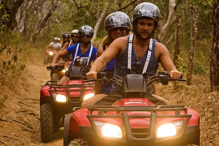 Close view of riders in helmets and straps on red ATVs driving along a dirt trail